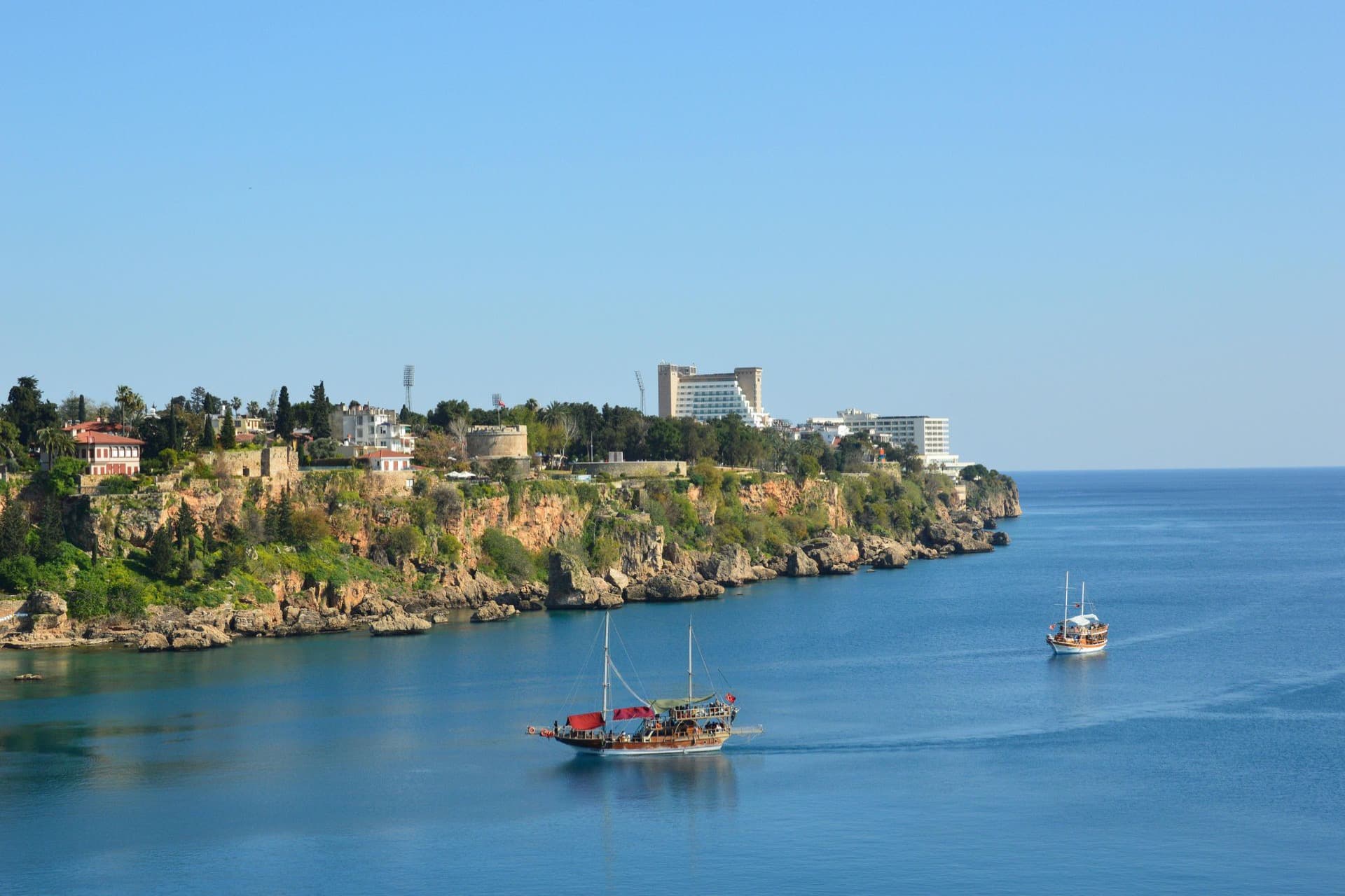 Cliffs of Antalya's old town with tour boats sailing in the bay.